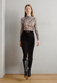 Top à manches longues avec un motif zèbre en beige et noir, associé à une jupe crayon noire et des bottes noires jusqu'aux genoux à bout pointu.