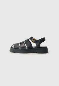 Zwarte leren sandalen met kruislings gespen, open teen ontwerp, een stevige rubberen zool en een gouden metalen gespaccent aan de zijkant.