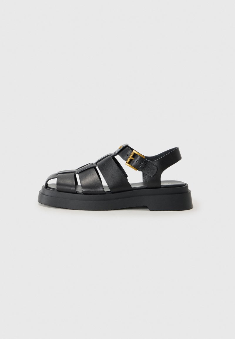 Zwarte leren sandalen met kruislings gespen, open teen ontwerp, een stevige rubberen zool en een gouden metalen gespaccent aan de zijkant.