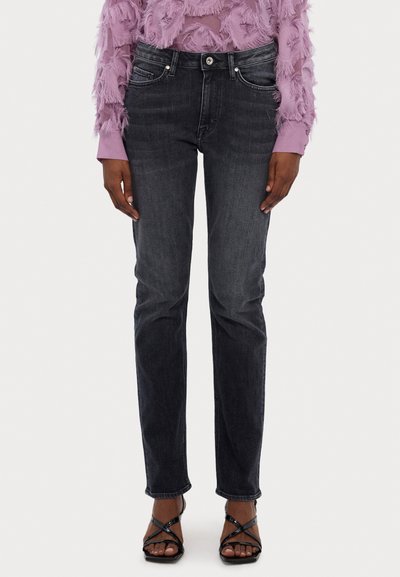 Vaqueros ajustados gris oscuro con bolsillos frontales, cremallera y cierre de botón metálico. Combinados con sandalias negras de tiras y una blusa de lavanda texturada.
