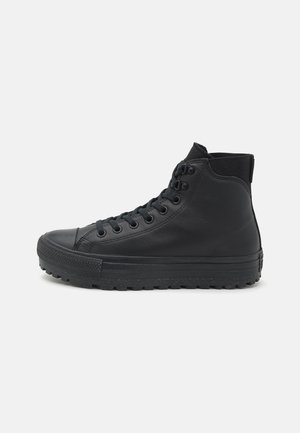 Baskets montantes noires avec semelle en caoutchouc texturée, lacets à l'avant et dessus en cuir lisse, vues de côté sur fond blanc.