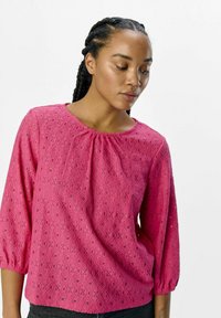 Blouse rose à manches trois quarts, ornée de motifs texturés en diamants et d'une encolure froncée. Tissu doux et léger.