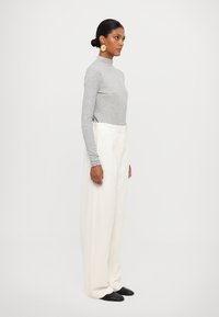 Grey long-sleeve turtleneck top paired with high-waisted white wide-leg trousers. Black pointed-toe shoes and large gold earrings complete the look.