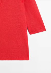 Czerwony sweter z dzianiny o długości rękawów do połowy przedramienia, z gładką fakturą oraz ściągaczami na mankietach i u dołu. Prosty wzór bez wzorów ani ozdób.