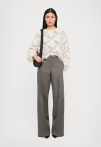 Ľahký, textúrovaný krémový top s detailmi fringu, v kombinácii so sivými nohavicami s voľným strihom a jemným vzorom houndstooth. Čierna crossbody taška.