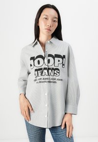 Stripet skjorte med knapper i lys grå med fet svart tekst "JOOP! JEANS" på fronten. Har krage og avslappet passform. Kombinert med blå denim.
