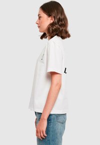 T-shirt en coton blanc à manches courtes, avec une coupe décontractée et des accents imprimés noirs à l'avant et à l'arrière. Jean en denim avec un lavage clair.