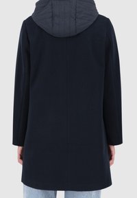 Námořnický kabát s prošívanou kapucí, rovný střih a dlouhý rukáv. Látka působí hladce s minimálním zdobením na zadní straně.