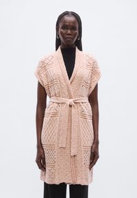 Πλεκτή ζακέτα σε ανοιχτό ροζ με υφή, ανοιχτό μπροστινό μέρος και δέσιμο στη μέση. Κοντά μανίκια και τσέπες σε κάθε πλευρά.