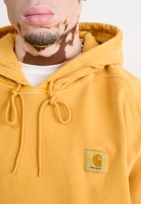 Hoodie jaune en coton doux avec une poche avant, doté de cordons de réglage et d'un patch logo carré sur la poitrine.