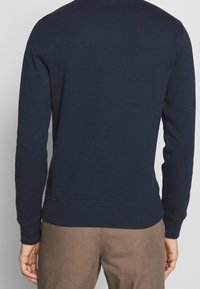 Námořnická modrá bavlněná mikina s dlouhými rukávy, žebrovanými manžetami a pasem. Hladká textura bez viditelných grafických prvků či vzorů.