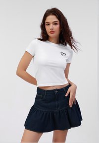 White cropped t-shirt with black heart design, paired with a dark denim flared skirt featuring a ruffled hem and front pockets.