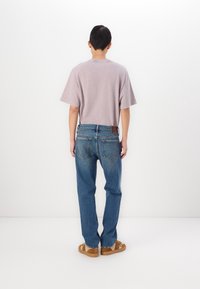 Camiseta de color púrpura claro con mangas cortas, combinada con jeans de mezclilla azul con un ligero desgaste y bolsillos traseros. Zapatillas sin cordones de color marrón.