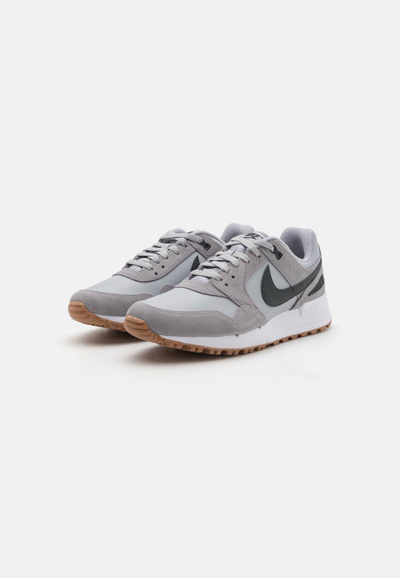 Baskets de sport grises avec un mélange de daim et de matériaux synthétiques, présentant un logo Nike gris foncé, une semelle intermédiaire blanche et une semelle extérieure en caoutchouc beige.