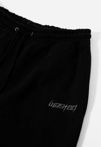 Schwarze Sweatpants aus Baumwolle haben einen elastischen Bund, einen Kordelzugverschluss und ein strukturiertes Logo in Grau auf der linken Vorderseite.