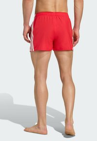 Rote Schwimmshorts mit einem bequemen elastischen Bund, weißen Seitenstreifen und einem kurzen, locker geschnittenen Design. Glattes, leichtes Material.