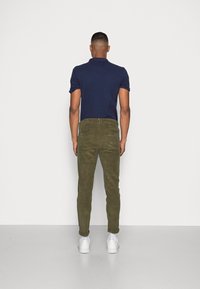 Navy polo shirt, olive green corduroy pants, white sneakers. Fit is slim, pants feature rolled cuffs and back pockets. Plain background.