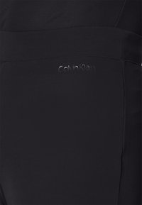 Černé legíny Calvin Klein s hladkým a elastickým materiálem, vysokým pasem a decentním logem značky embosovaným na boku.