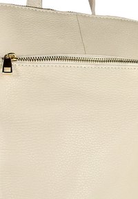 Beige leren tas met textuur, voorzien van een horizontale gouden ritszak en bijpassende handvatten die zichtbaar zijn aan de bovenkant.