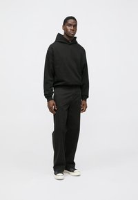 Black hooded sweatshirt and matching relaxed-fit pants, made of soft fabric. Features a kangaroo pocket and minimal design. White sneakers.