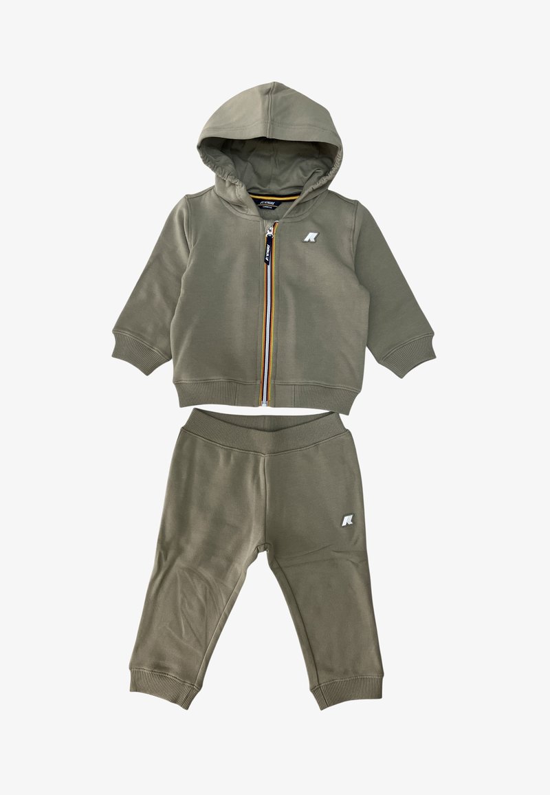 Tuta verde oliva con felpa con zip e pantaloni coordinati. Presenta polsini a coste, un logo sulla giacca e un rivestimento interno a contrasto.