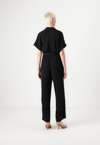 Svart jumpsuit med korte, rullede ermer, elastisk midje og bred benpassform. Smoother materiale med en avslappet passform, ingen synlige mønstre eller hardware.