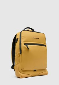 Mochila amarilla hecha de material texturizado, con un bolsillo frontal con cremallera, detalles en negro y una base estructurada para mayor estabilidad.