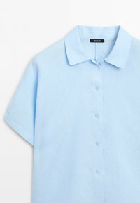 Chemise bleu clair à manches courtes avec col et cinq boutons sur le devant, présentée sur fond blanc.