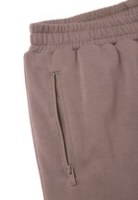 Lichtbruine joggerbroek van zacht materiaal, met een elastische tailleband en een zijzak met rits en bijpassende hardware.