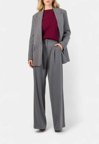 Pantaloni grigi a gamba larga abbinati a un blazer grigio, indossati su un top bordeaux. Tessuto morbido con design strutturato e vestibilità rilassata.
