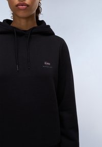 Zwarte hoodie met een relaxte pasvorm, gemaakt van zachte stof. Heeft een klein geborduurd logo en een trekkoord bij de hals.