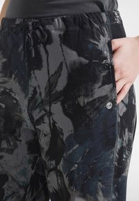 Czarno-szare wzorzyste spodnie dresowe z elastycznym stanem, sznurkiem oraz bocznymi kieszeniami. Zdobione abstrakcyjnymi motywami kwiatowymi w odcieniach niebieskiego.