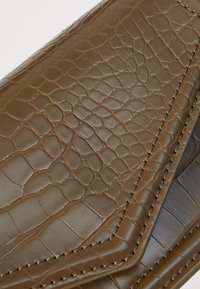 Bruine leren clutch met een geëtste krokodillenpatroon, met gladde randen en contrasterende stiksels. Ontwerp met gesloten klep.