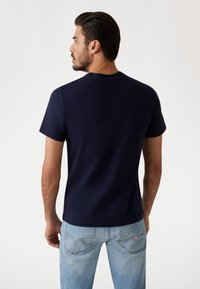 Navy blue short-sleeve t-shirt, round neck, cotton material, with a relaxed fit, paired with light blue denim jeans featuring back pockets.