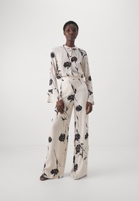 Set a due pezzi con stampa floreale in crema e nero, caratterizzato da maniche lunghe, polsini svasati, pantaloni a gamba larga e vita sagomata. Tessuto morbido e leggero.