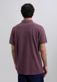 Polo de manga corta en un color malva apagado. Fabricado en un tejido suave con un cuello clásico y un acabado sutilmente texturizado.