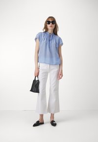 Haut bleu clair à manches courtes avec col froncé, associé à un pantalon blanc évasé, des mules noires et un petit sac à main noir.