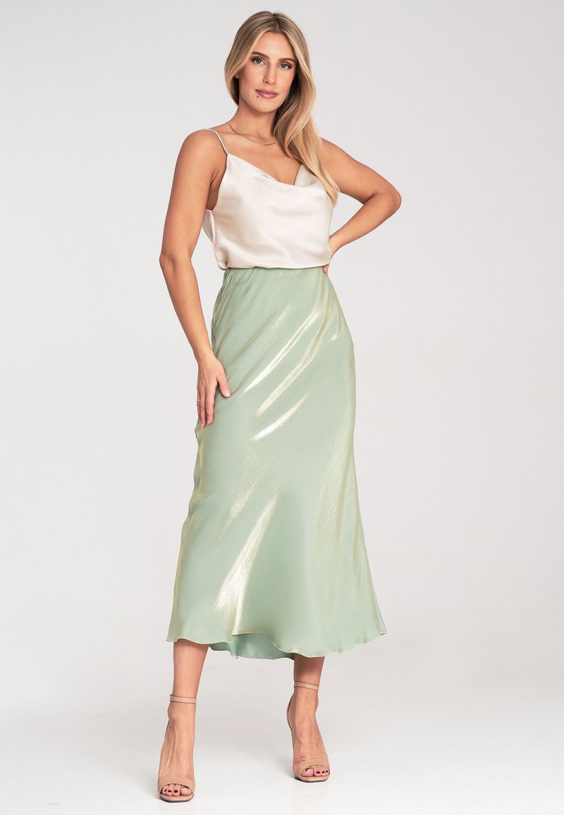 Satin-Camisole in Elfenbein, kombiniert mit einem fließenden Rock in Mintgrün, der einen metallischen Glanz und eine A-Linien-Form aufweist. Riemchen-High Heels in Nude runden den Look ab.