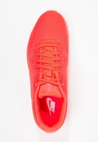 Červené Nike tenisky s perforovaným designem, plochými šňůrkami a polstrovaným límcem. Mají texturovaný svršek a kontrastní podšívku.