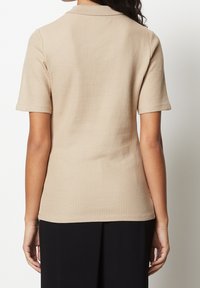 Beige ribbet polo shirt med kort ærme og krave, med en tekstureret overflade og en tætsiddende pasform, der går til taljen.