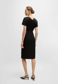 Juodas midi suknelė trumpomis rankovėmis ir V formos dekolte. Lycra audinys, prigludęs siluetas, paslėptas užtrauktukas nugaroje, iki kelių ilgio. Elegantiškas dizainas.