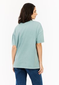 Lichtgroene oversized T-shirt met korte mouwen, gemaakt van zachte stof. Heeft een ronde halslijn en een relaxte pasvorm, gecombineerd met blauwe spijkerbroek.