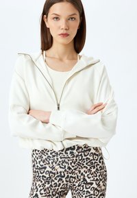 Witte zip-up sweatshirt met raglanmouwen en een hoge kraag, gecombineerd met aansluitende leggings met een luipaardprint.