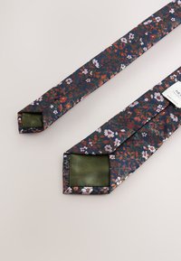 Kravata s květinovým vzorem v námořnické modři s růžovými, oranžovými a bílými květy. Konce mají jednobarevný zelený saténový povrch. Texturovaná tkanina.