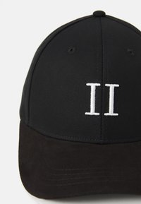 Gorra negra con un diseño estructurado, que presenta un "II" bordado en blanco en la parte frontal y un visera de ante negro. Material de tela texturizada.