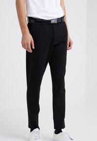 Pantalons noirs taillés en tissu lisse, présentant une coupe droite avec des détails de couture subtils à l'avant, associés à une ceinture noire élégante.
