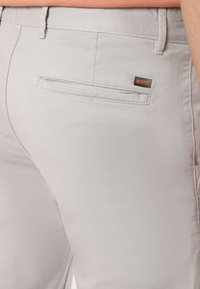 Pantalon gris clair sur mesure avec une texture lisse, doté d'une poche arrière et d'une petite étiquette "BOSS" noire et orange.