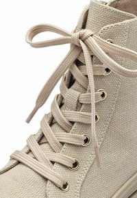 Baskets montantes en toile beige avec surface texturée, œillets dorés et lacets classiques. Embout renforcé et lacets ton sur ton.