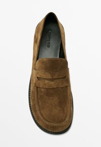 Mocassini in suede marrone con una texture liscia, punta arrotondata e una fascia decorativa frontale; suola in gomma nera con un delicato motivo di scolpitura.