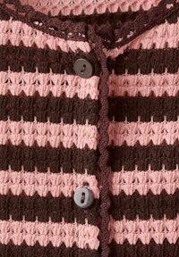 Gros plan d’un tissu tricoté rayé rose et brun foncé avec deux boutons noirs et une bordure ondulée brun foncé le long du bord.